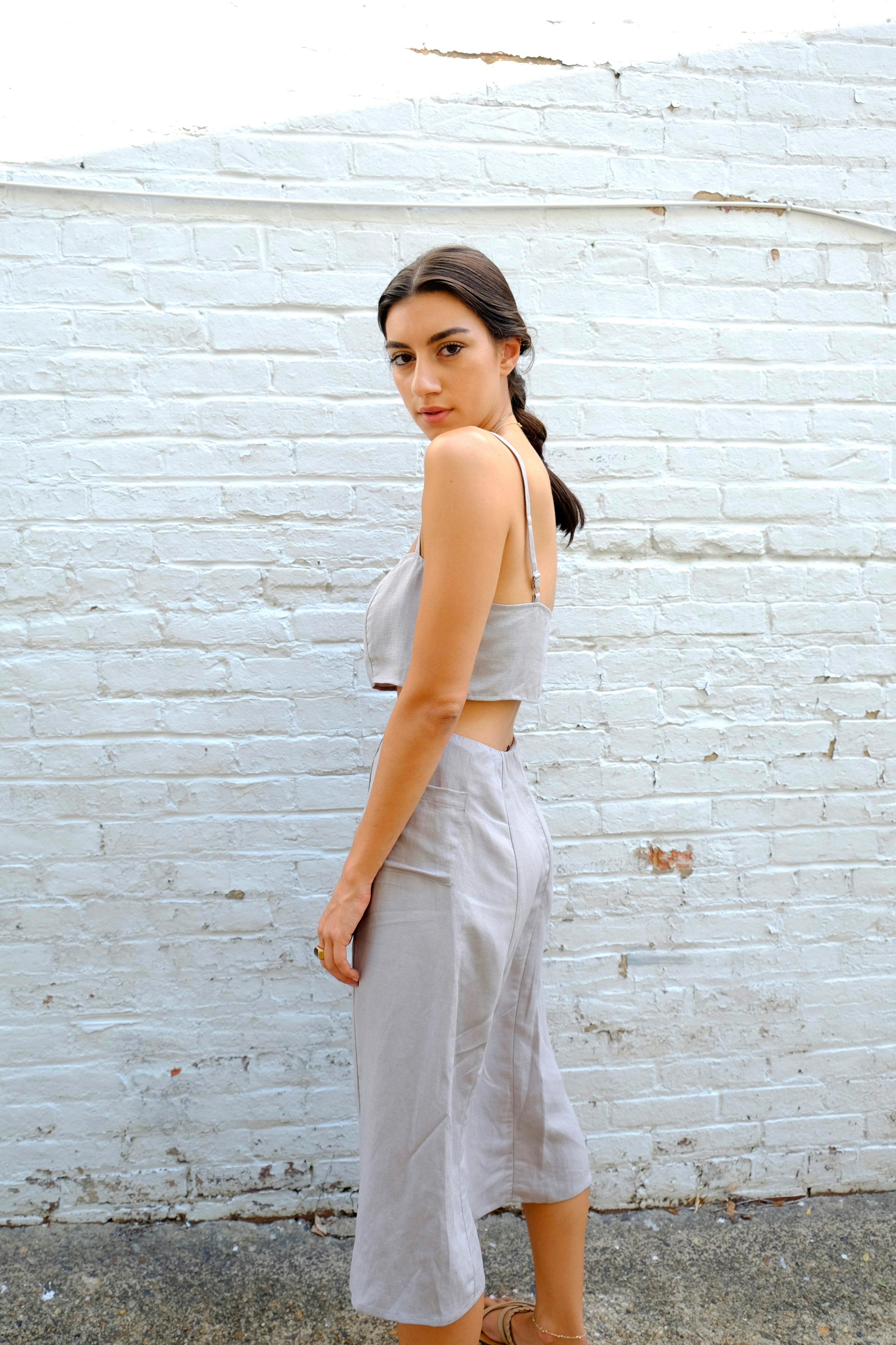 woman in white tank top and white pants standing beside brick wall